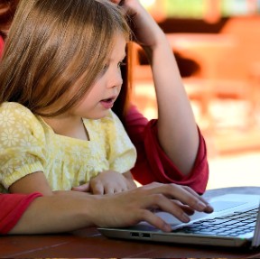 A child on a laptop being supervised by an adult